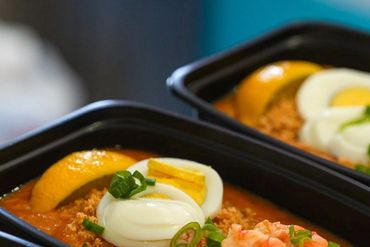 Close-up of shrimp and egg-topped seafood dish in black containers.