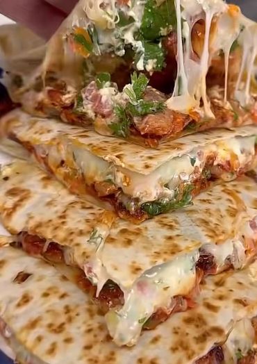 Close-up of cheesy quesadilla slices with herbs and melted cheese.