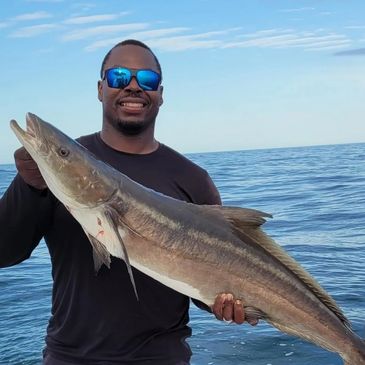Man holding a large fish on a boat with ocean background.