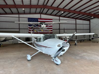 Small white airplane inside a hangar with an American flag in the background.