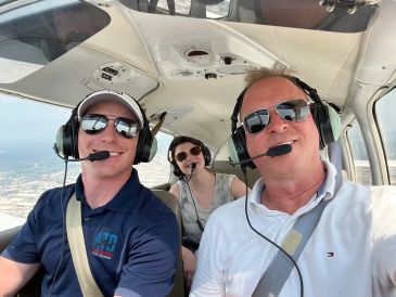 Three people wearing headsets in a small airplane cockpit.