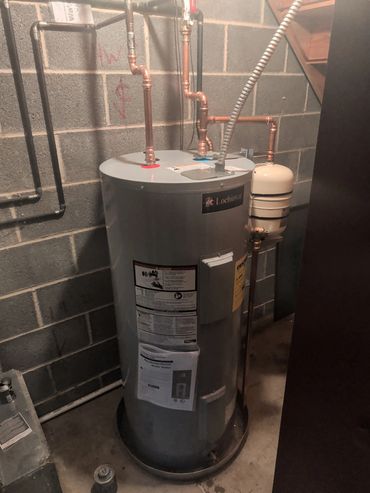 Electric water heater installed in a basement with copper piping.