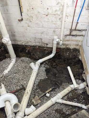 PVC plumbing pipes and a shovel on gravel in a basement under construction.