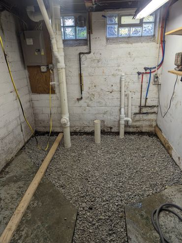Basement with plumbing pipes and gravel floor preparation.