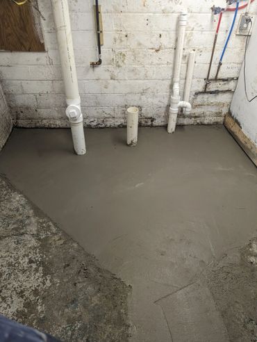 Newly poured concrete floor with exposed plumbing pipes in a basement.