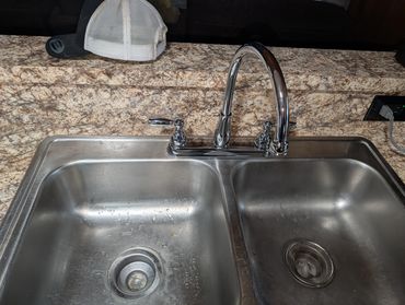 Stainless steel double kitchen sink with chrome faucet and hats on granite countertop.