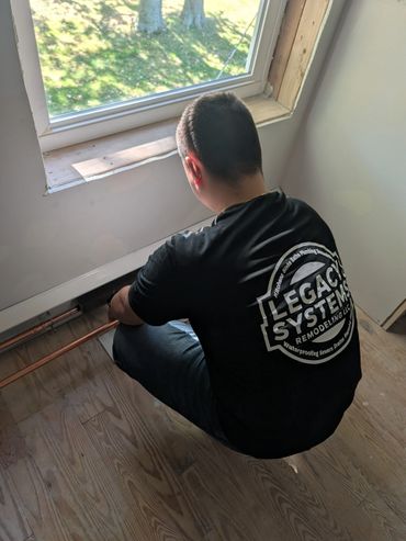 Worker in a Legacy Systems shirt installs copper pipes by a window.