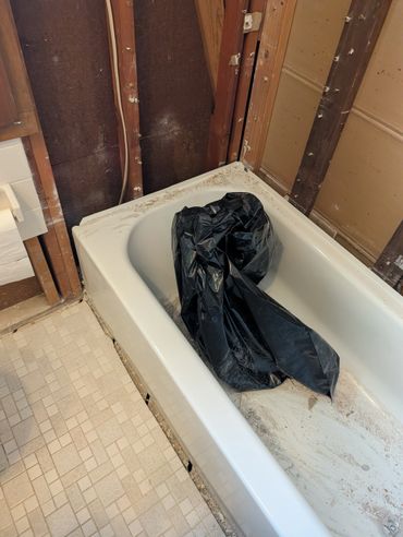 Bathtub in a partially demolished bathroom with exposed wall studs and debris.