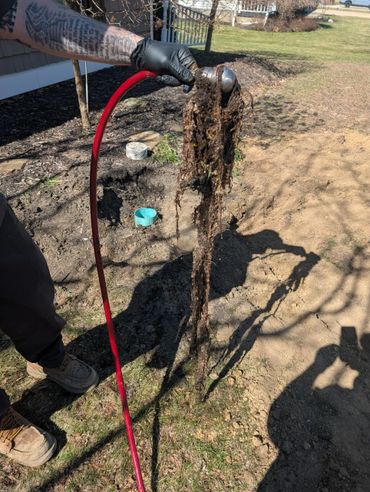 Person holding a red hose clogged with roots and debris outdoors.