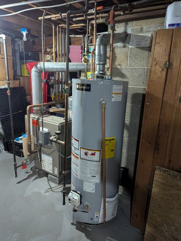 Water heater and furnace setup in a basement with visible pipes and warning labels.
