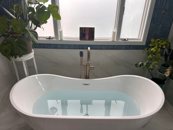 Modern bathroom with a filled white bathtub and green plants.