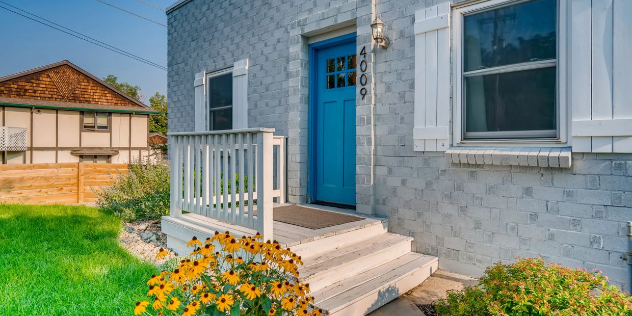 Blue front door on a gray brick house with white trim and yellow flowers.