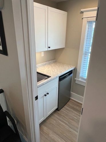 Compact kitchen area with white cabinets, marble countertop, and stainless steel mini fridge.