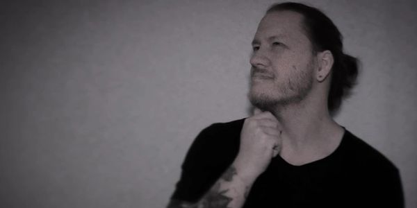 Man with tattoos and a beard, looking thoughtfully to the side.