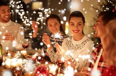 Friends celebrating with sparklers around a festive holiday dinner table.