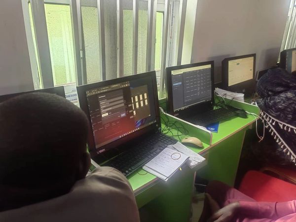 People working on laptops in a room with green desks and barred windows.