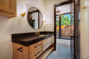 A wooden bathroom counter with a black sink and a round mirror