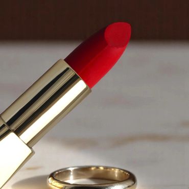 Red lipstick and gold ring on a marble surface.