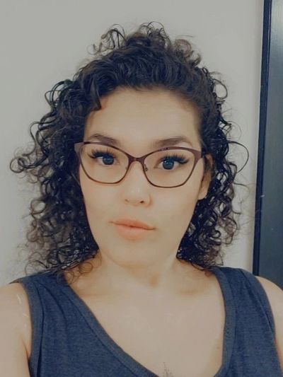 Woman with curly hair and glasses taking a selfie.