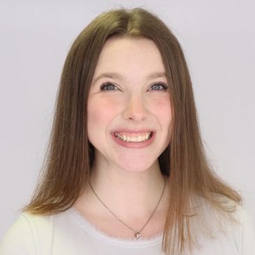 A young woman smiling with long straight hair and a white top.