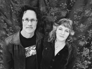 Black and white photo of a man and woman standing together against a floral backdrop.