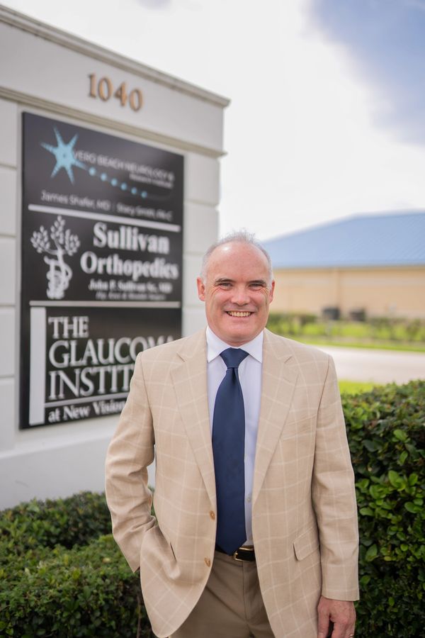 Smiling man in beige suit standing outside medical office.