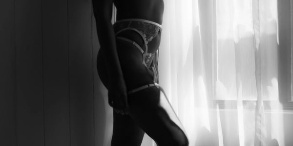 Silhouette of a woman in lingerie standing by a window with sheer curtains.