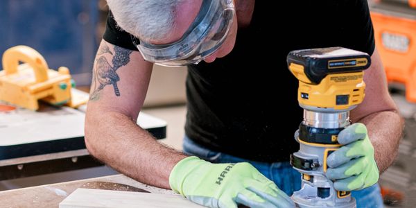 Man using a power tool to shape wood in a workshop.