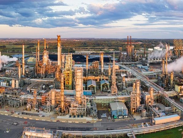 Large industrial refinery complex with numerous towers and pipes under a partly cloudy sky.