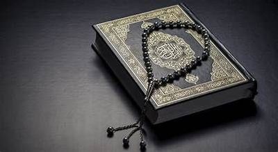 A Quran with a black prayer bead necklace placed on it.