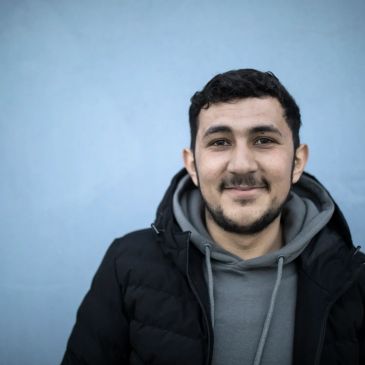 Smiling young man in casual winter clothes against a blue background.