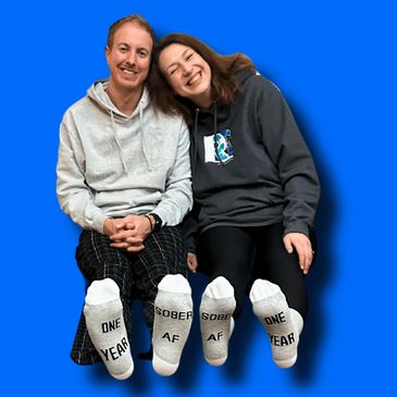 Couple sitting together in socks that read "Sober AF" and "One Year."