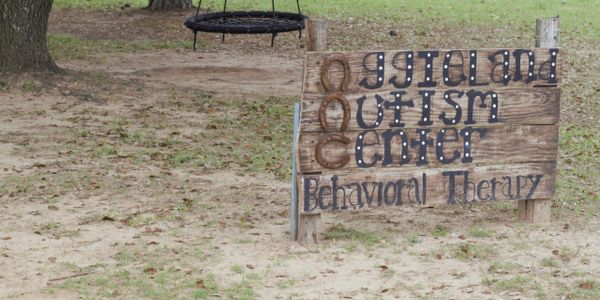 An Aggieland Autism Center sign made out of wood with black letters.