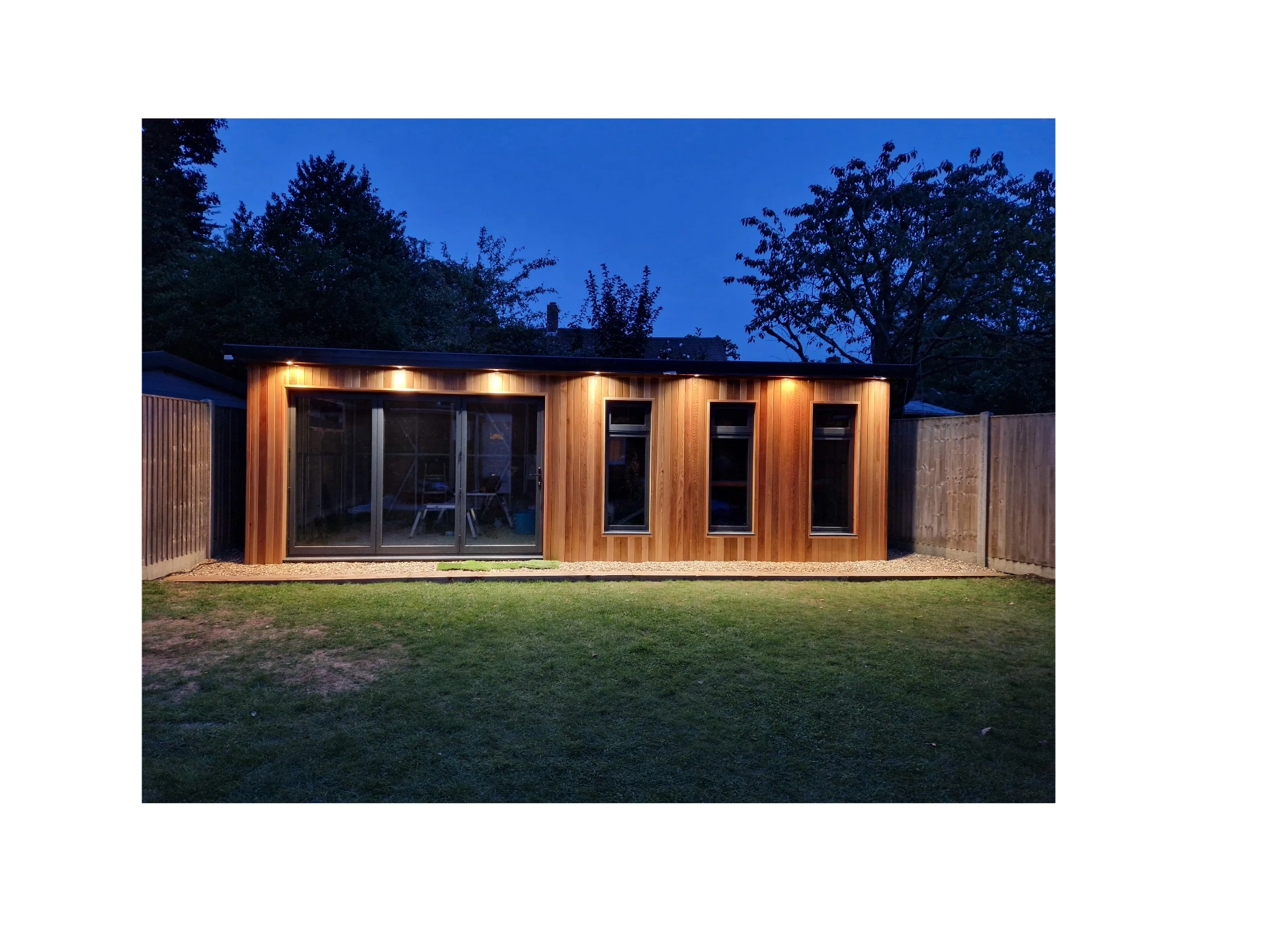 Modern wooden garden studio illuminated at night with warm lights.