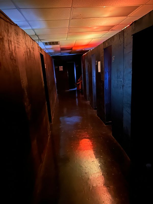 Dimly lit corridor with numbered dark wooden doors and colorful ceiling lights.
