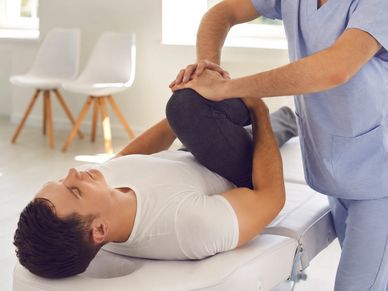 A physical therapist stretches a man's leg during a therapy session.