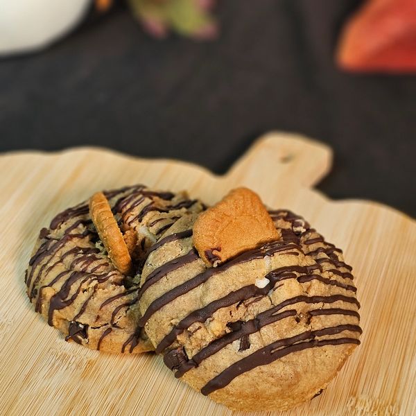 Two cookies drizzled with chocolate and topped with small cookies on a wooden board.