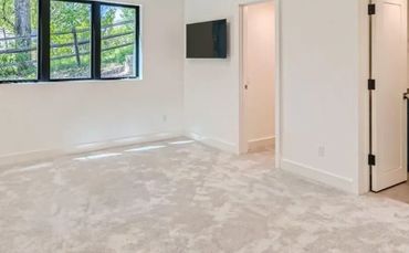 Bright empty bedroom with large window and carpeted floor.