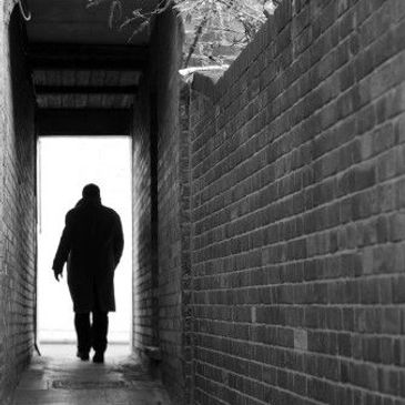 A silhouette of a person walking through a narrow brick alleyway.