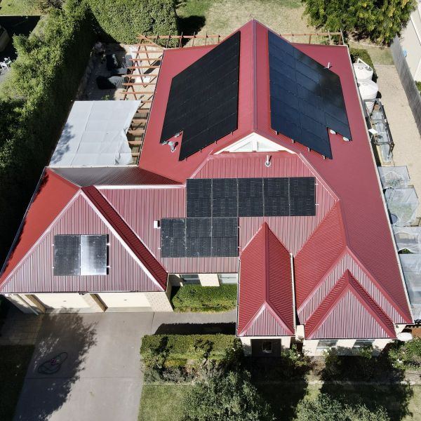 Aerial view of a house with red roof and multiple solar panels installed.