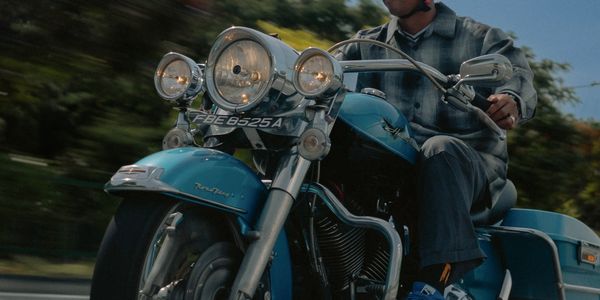 Man riding a blue vintage motorcycle wearing a helmet and sunglasses.