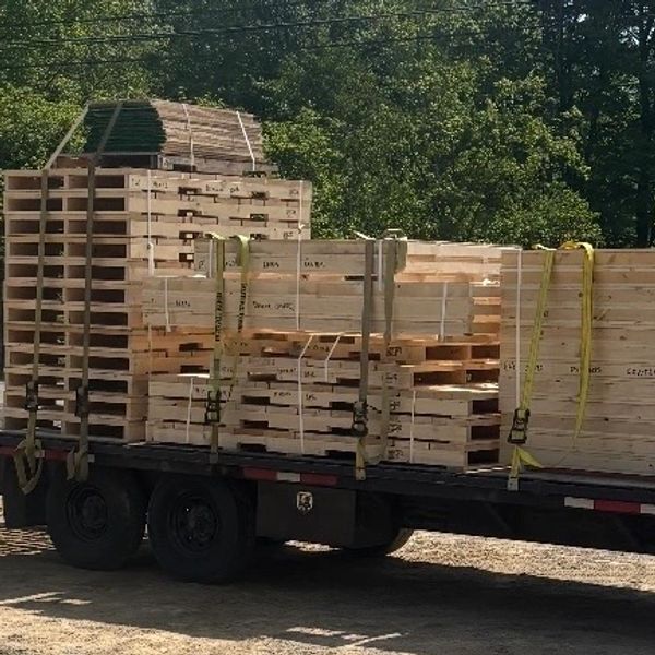Stacked wooden pallets and crates secured on a trailer outdoors.