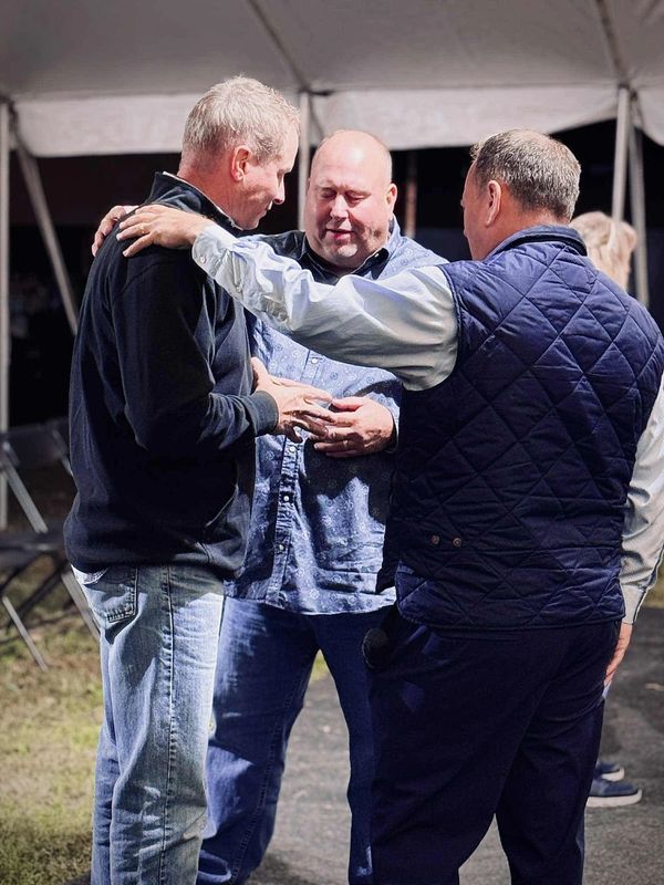 Three men engaged in a heartfelt conversation under a tent.