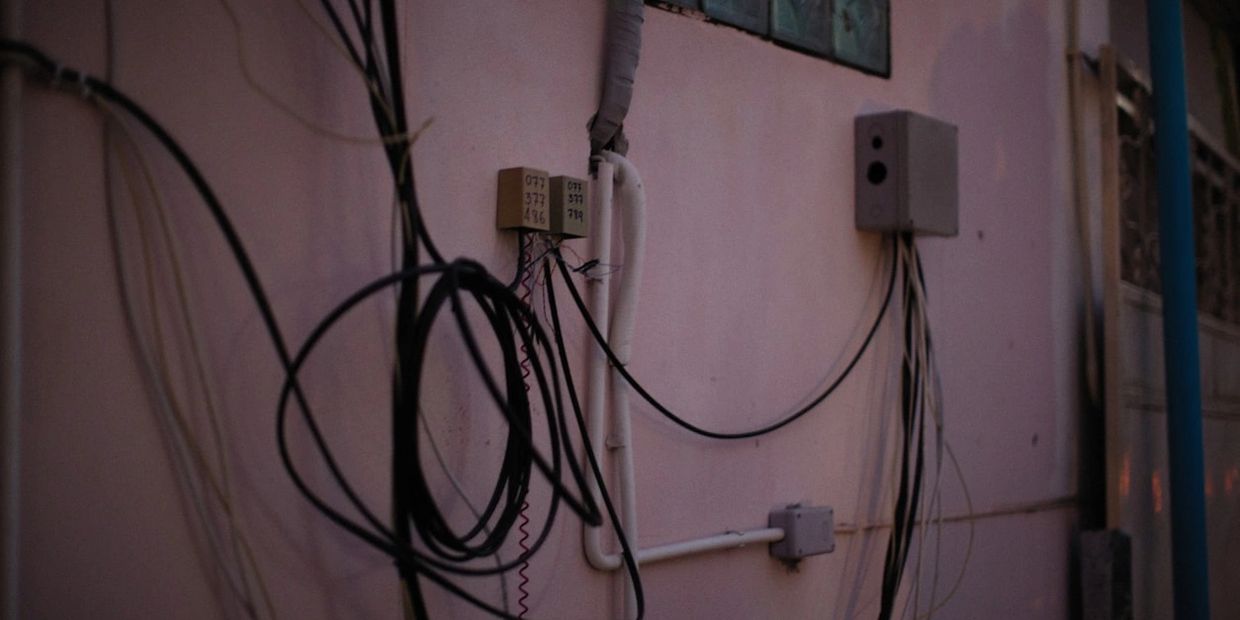 Tangled black wires on a pink wall with electrical boxes.