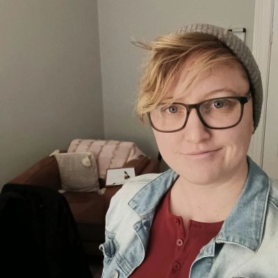 Person with glasses and beanie in a cozy room.