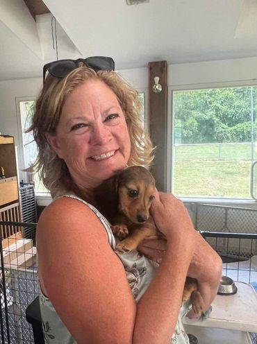 Woman smiling and holding a small brown puppy indoors.