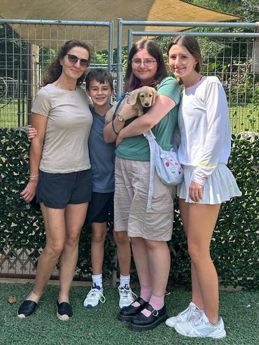 Four people stand together outside, one holding a small dog.