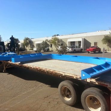 Large blue metal frame on a flatbed truck outside a warehouse.