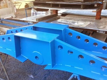 Large blue metal structure with holes, supported on stands in a workshop.