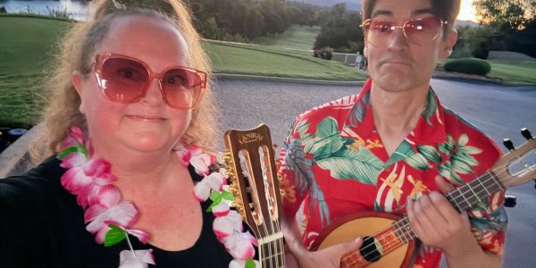 Two people wearing sunglasses and holding string instruments.